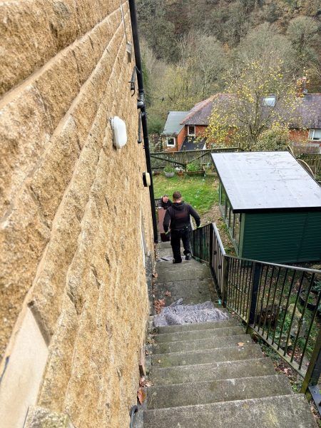 Piano mover carrying equipment down a steep flight of stone steps to a rural property